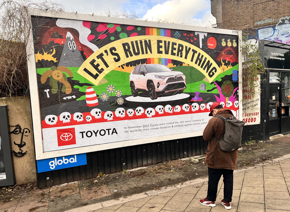 A man stands in front of a billboard. The board shows an SUV under a banner reading "Let's Ruin Everything". In the bottom left corner is a Toyota logo.