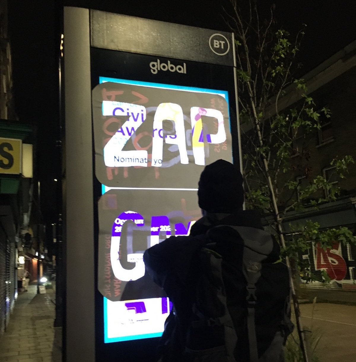 A person with their back to the camera puts a poster on a digital ad screen. the poster reads "ZAP Games"